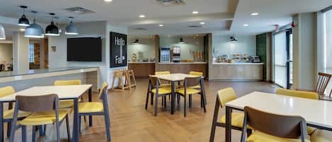 A modern dining area with multiple tables and chairs, a kitchen area with a chalkboard, and a large window providing natural light.
