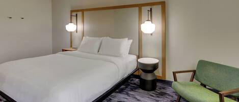 Une chambre d’hôtel avec un grand lit, un fauteuil vert et deux lampes de chevet.