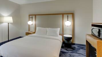 A hotel room with a large bed, bedside lamps, a wooden headboard, a small bedside table, a round black nightstand, and a microwave on a wooden cabinet.