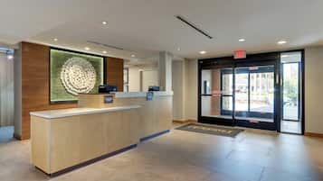 A reception desk with a modern design, a large decorative wall piece, and a glass door entrance with an exit sign.