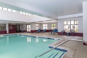 An indoor swimming pool with clear water, surrounded by lounge chairs and a tiled floor.