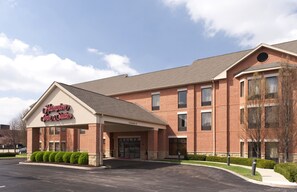 A Hampton Inn Suites building with a brick facade, a covered entrance, and a parking lot.
