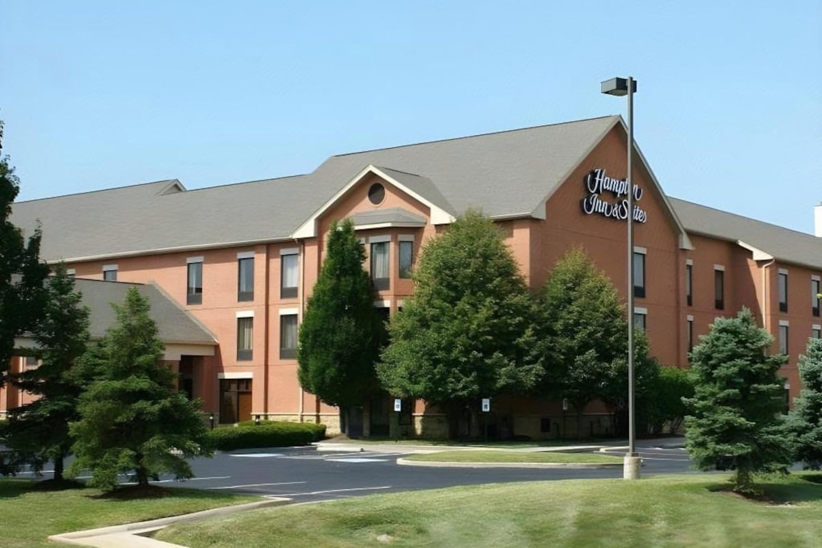 A hotel with a prominent sign, a driveway, and surrounding greenery.