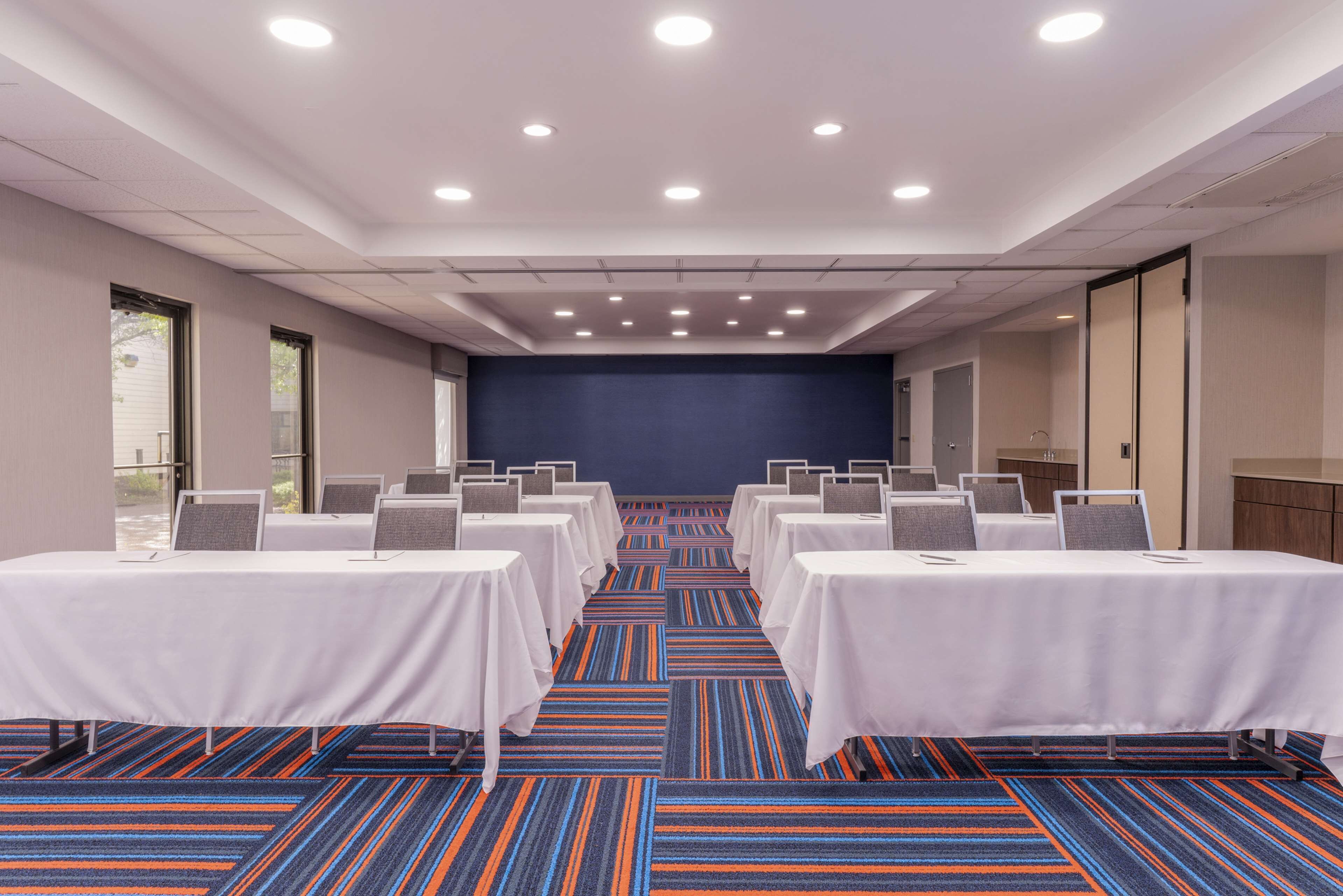 Une salle de conférence dotée de plusieurs tables et chaises, d’un tapis bleu et d’un plafond blanc avec des luminaires encastrés.