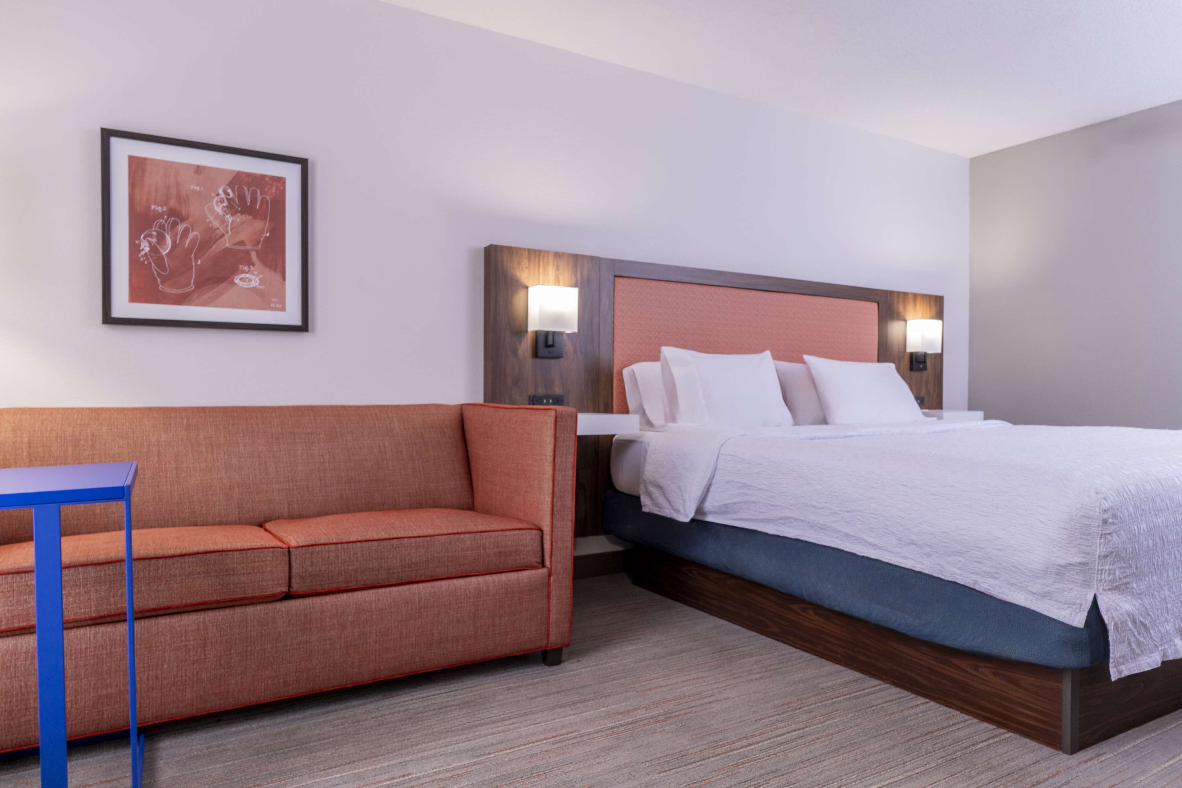 A hotel room with a bed, a sofa, and a framed artwork on the wall.