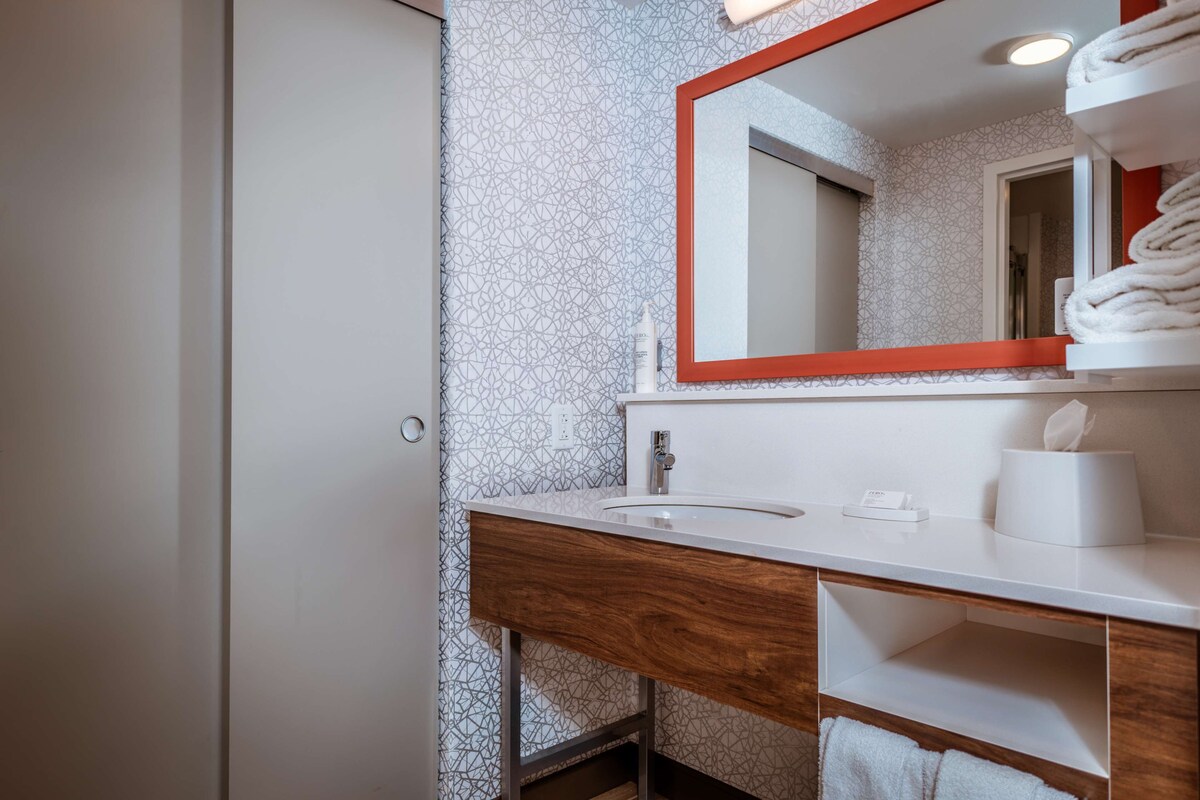 A bathroom with a white sink, wooden vanity, and a mirror with a red frame.