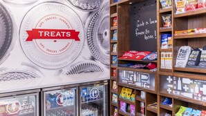 Ein Ladeninneres mit einem 'Treats'-Schild, Snackregalen und einer Tafel mit einer Willkommensbotschaft.
