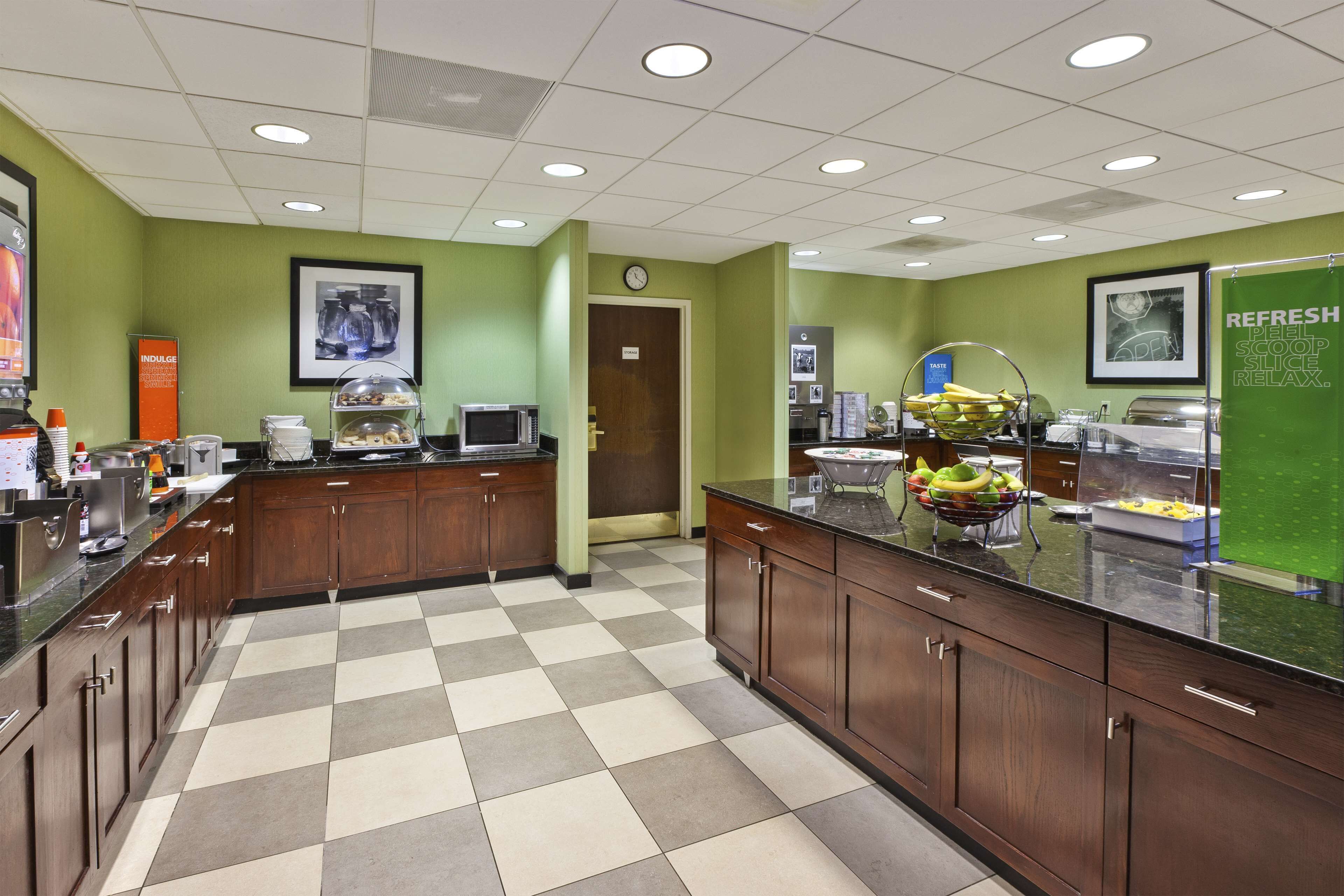 A clean, well-lit kitchen with a checkered floor, wooden cabinets, and various food items displayed on the counter.