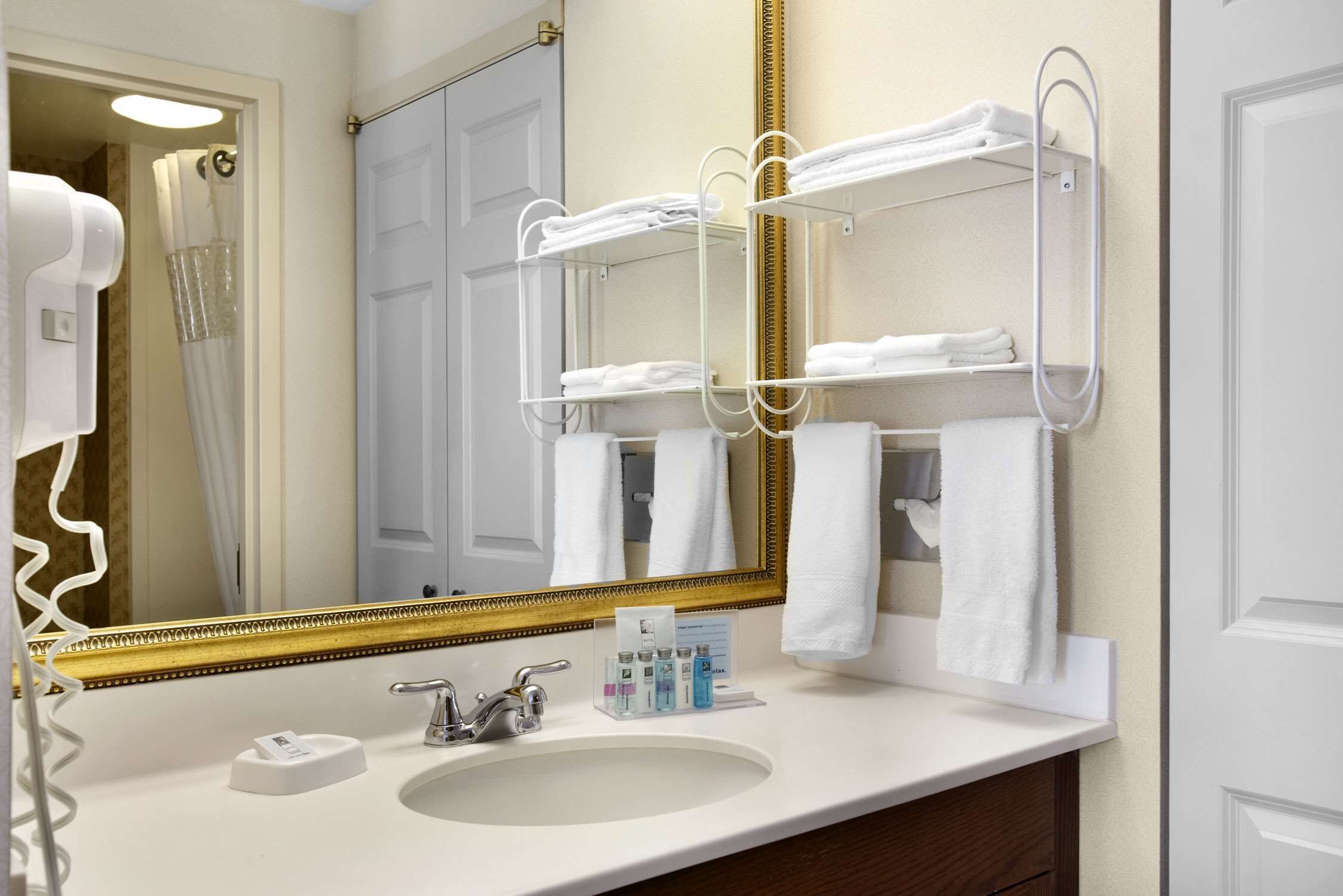 A bathroom with a white sink, a large mirror with a gold frame, and two towel racks with white towels.