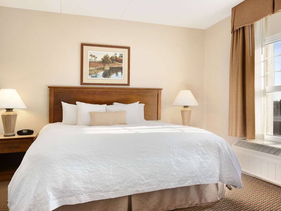 A hotel room with a large bed, two bedside tables with lamps, a framed picture on the wall, and a window with curtains.