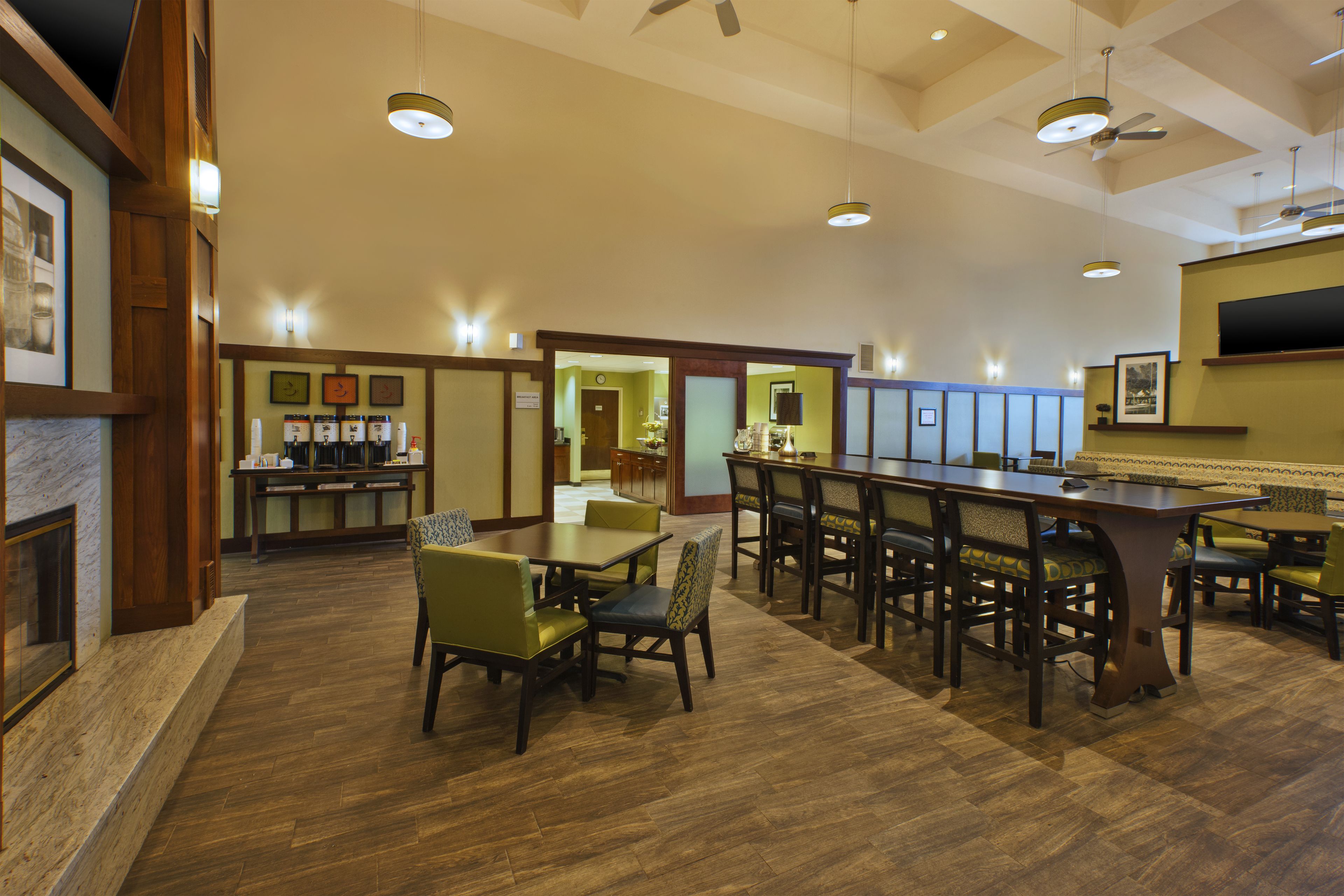 Un hall d’hôtel spacieux comprenant un bar, des tables et des chaises, et doté d’un plancher en bois et de ventilateurs de plafond.