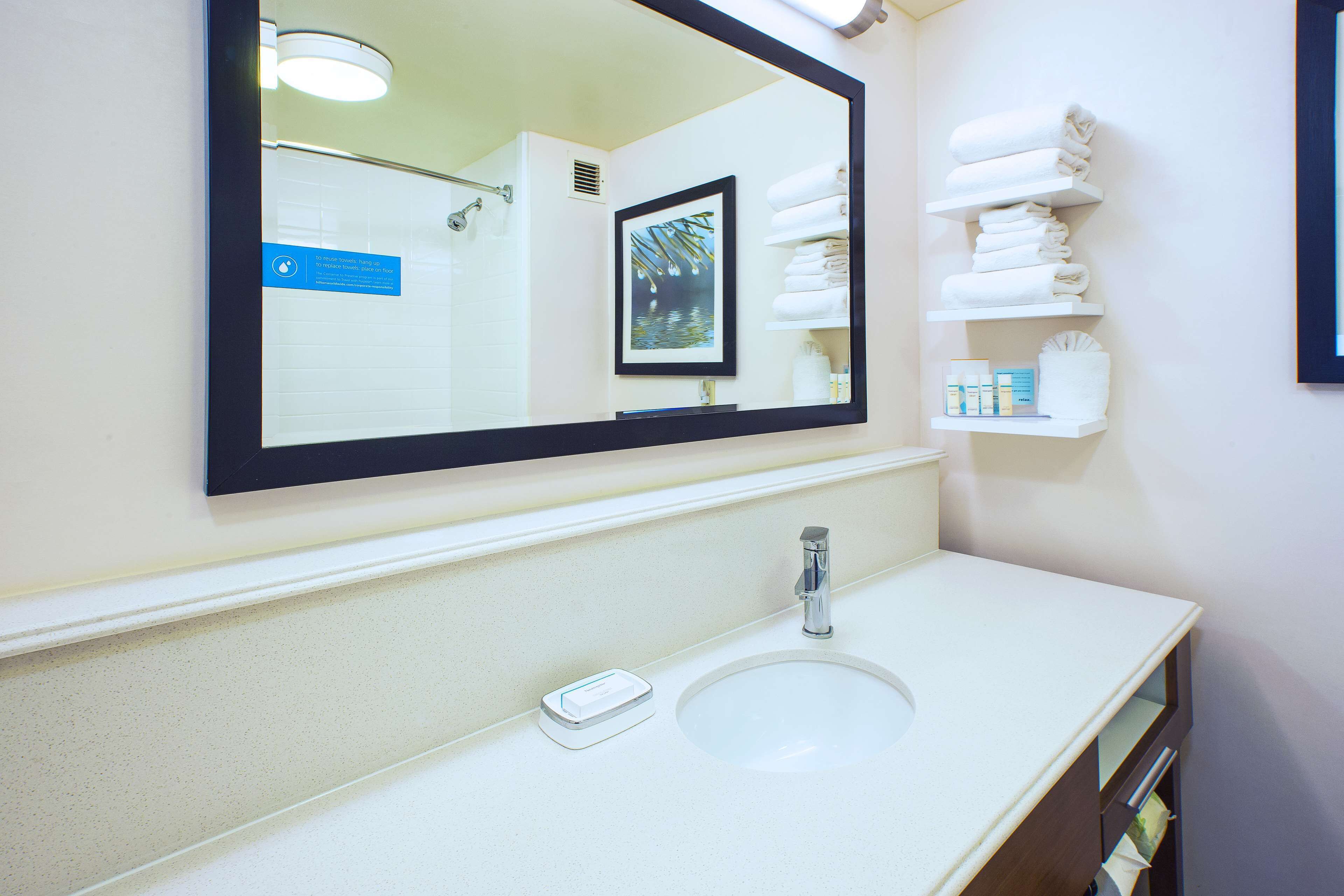 Un baño con lavamanos, espejo y toallero.