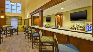 A bar area with wooden chairs, a long counter, and a television mounted above the bar.