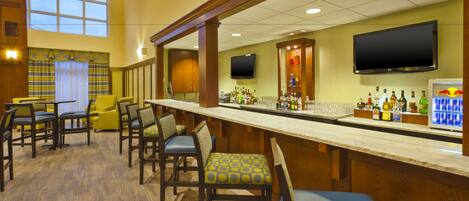 A bar area with wooden chairs, a long counter, and a television mounted above the bar.
