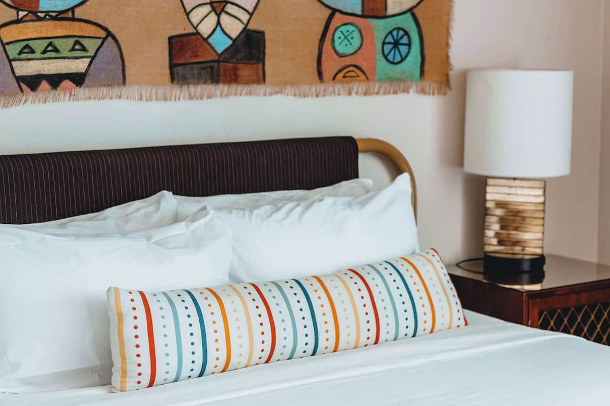 A bed with white linens, a colorful striped pillow, and a blanket with a star pattern.