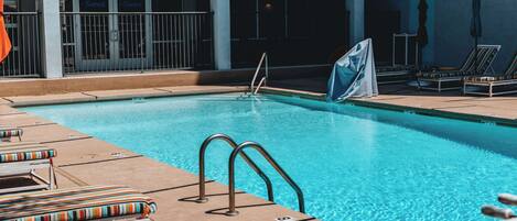 A swimming pool with lounge chairs and a covered area.
