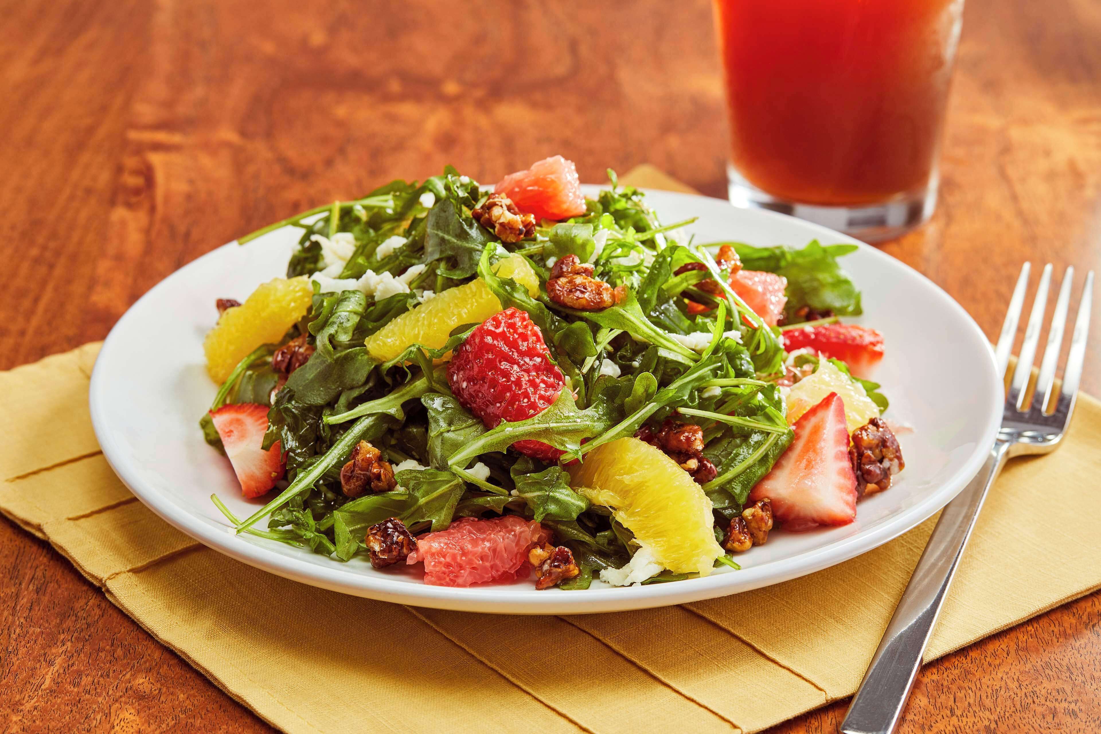 A plate of mixed greens salad with strawberries and orange segments on a wooden table.