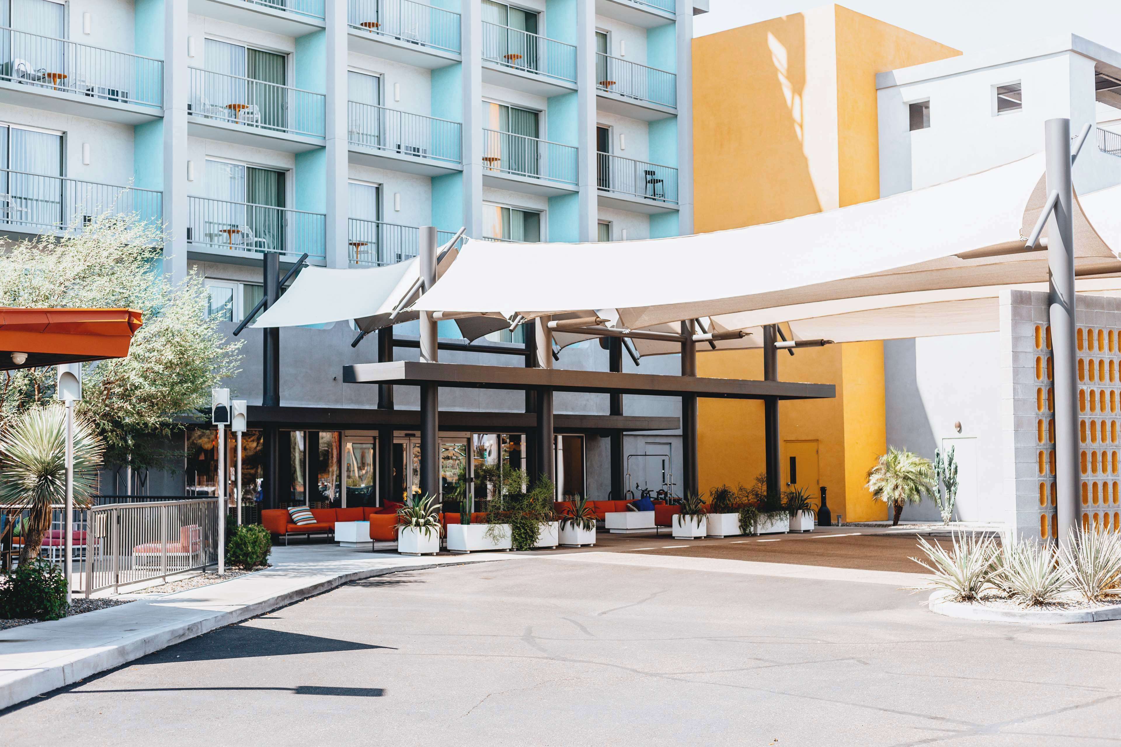 A modern hotel with a covered outdoor seating area, a pool, and a multi-story building with balconies.