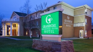 Een GrandStay Hotel met een opvallend groen bord, een verzorgd gazon en een klassiek gebouw.