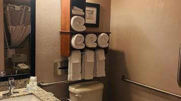 A bathroom with a toilet, a sink with a marble countertop, a towel rack with towels, a framed picture, and a mirror.