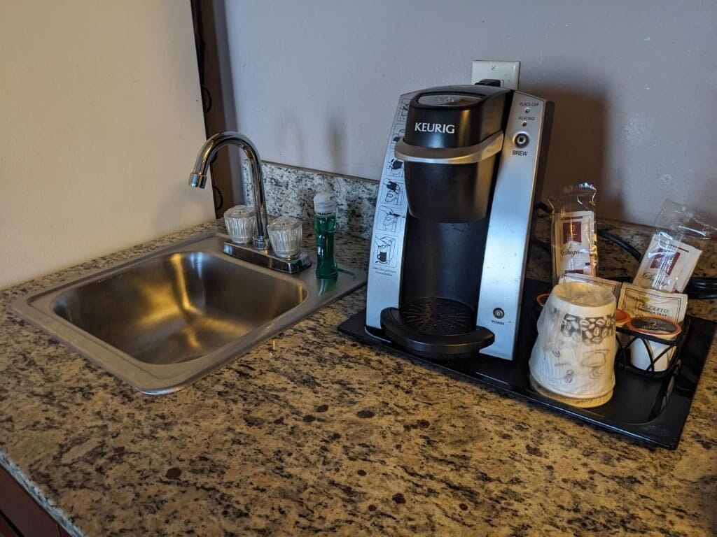 Una cocina con una cafetera Keurig, un lavamanos y una bandeja con una jarra de café y un vaso.