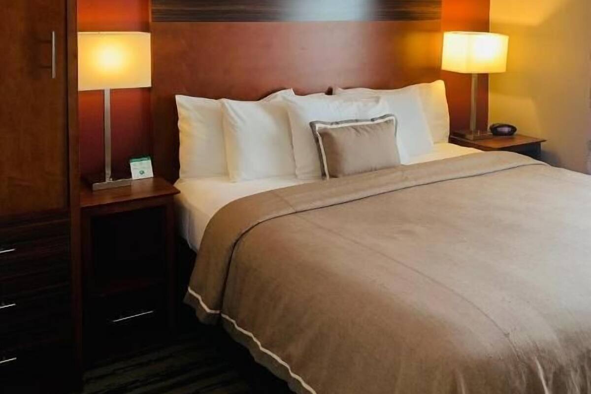 Une chambre d’hôtel avec un grand lit, deux lampes de chevet, une tête de lit en bois et une armoire.