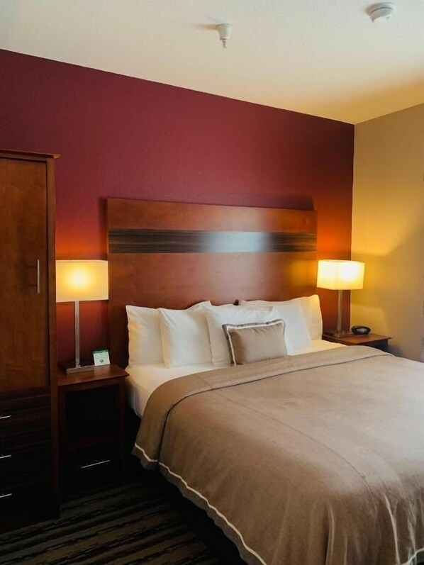 A hotel room with a large bed, two bedside lamps, a wooden headboard, and a wardrobe.