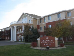 Das GrandStay Residential Suites Hotel mit markantem Eingang, überdachter Terrasse und begrüntem Vorgarten.
