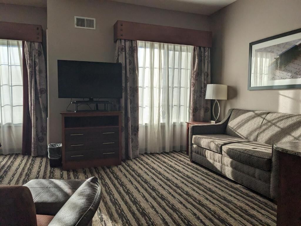 A hotel room with a television, a sofa, a lamp, and a patterned carpet.
