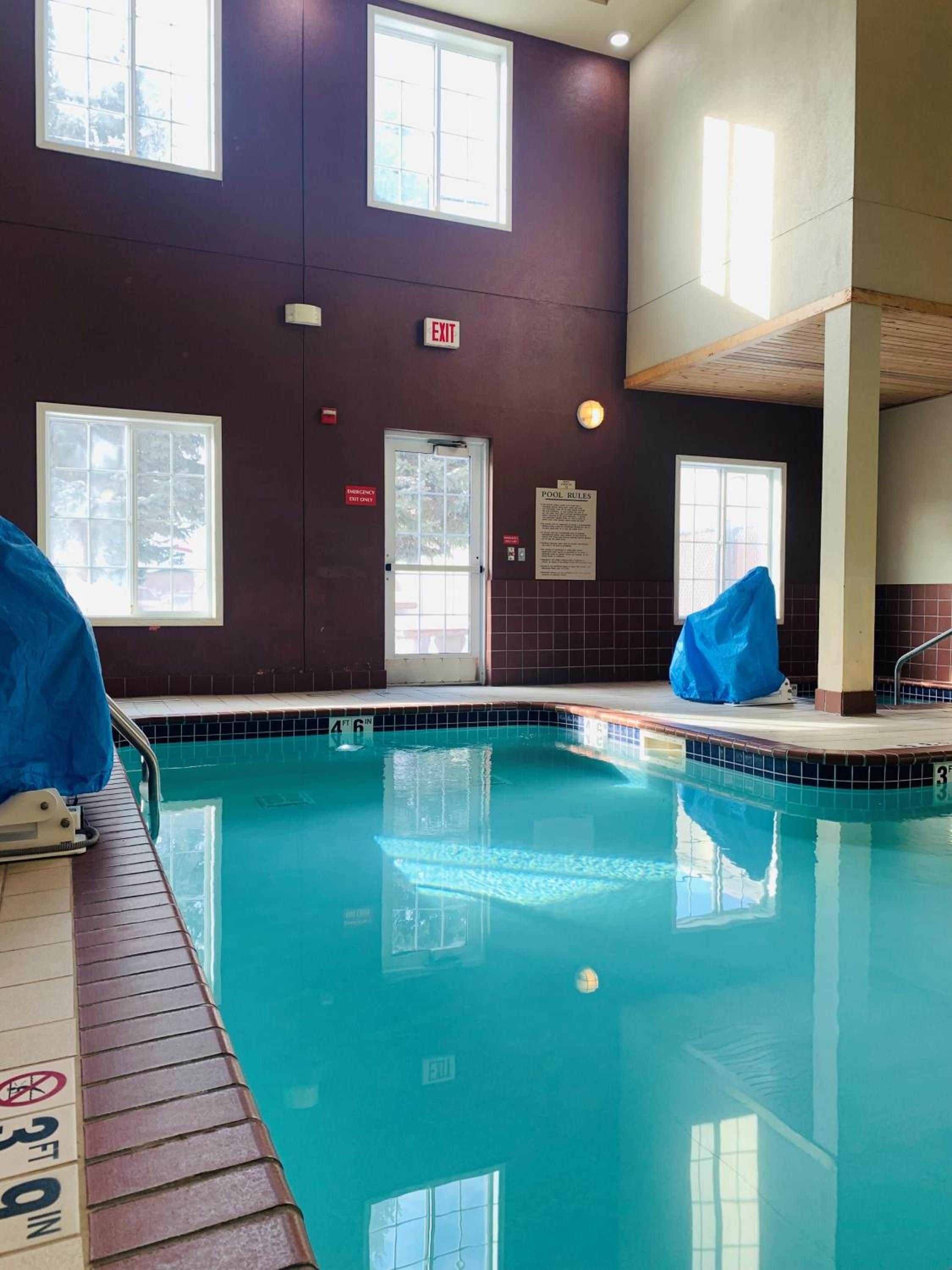 An indoor swimming pool with clear water, marked depth lines, and multiple windows providing natural light.
