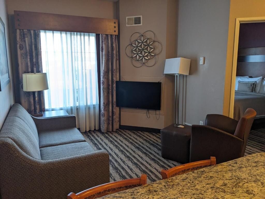 A hotel room with a sofa, a TV, a lamp, and a bed.