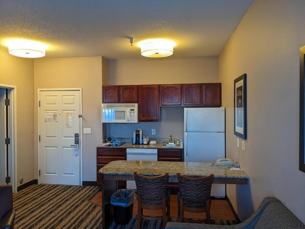 A compact kitchen with wooden cabinets, a microwave, a refrigerator, and a granite countertop.