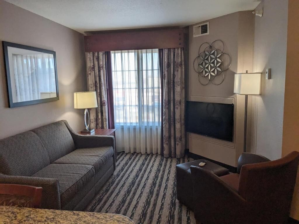 A hotel room with a sofa, a TV, a lamp, and a patterned carpet.