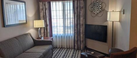 A hotel room with a sofa, a TV, a lamp, and a patterned carpet.