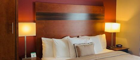Habitación de hotel con una cama grande, dos lámparas de noche, un cabecero de madera y una mesita de noche con lámpara.