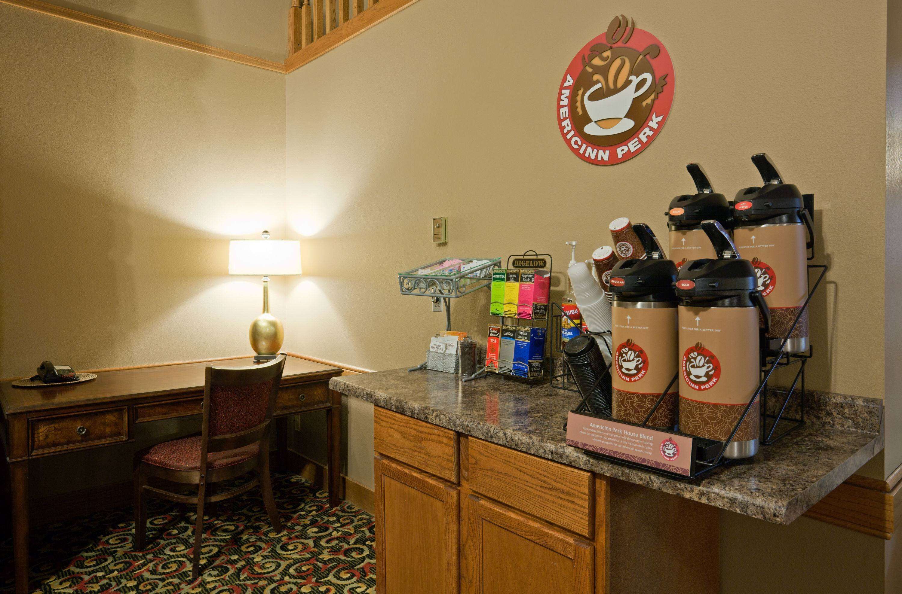 A hotel kitchen with a coffee station, a desk, and a chair.