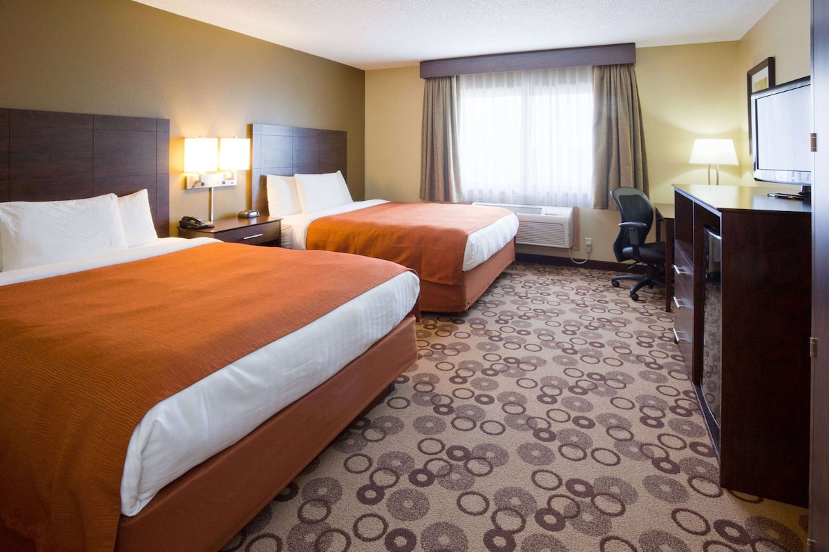 A hotel room with two beds, a desk, a chair, a television, and a window with curtains.