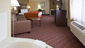 Une chambre d’hôtel comprenant un lit, un canapé, un bureau, une télévision, une cheminée et une salle de bain avec une baignoire.