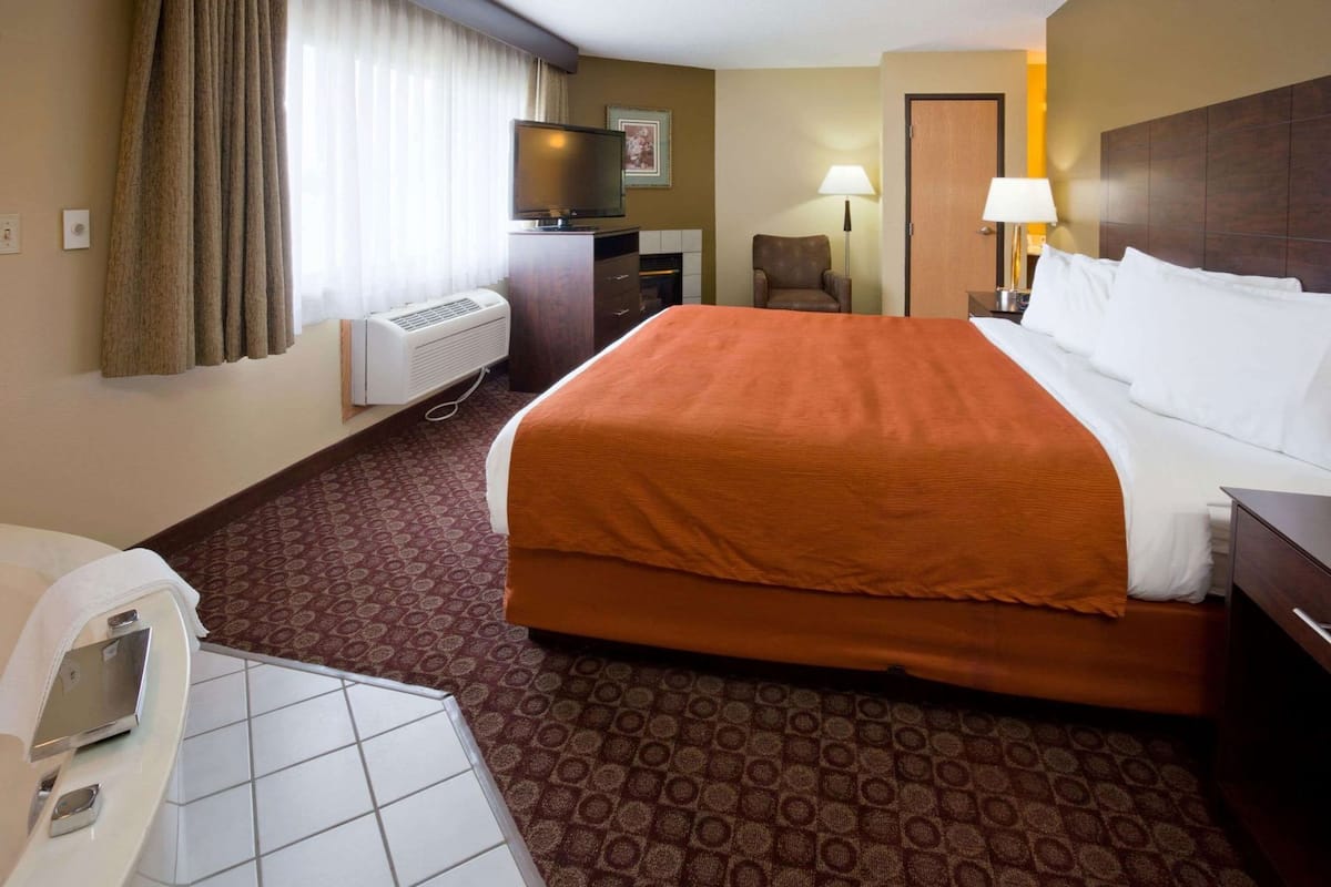 A hotel room with a bed, a desk, a chair, a TV, a lamp, and a bathroom.