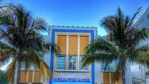 Hotel Ocean Five med blå markise, palmer og en parkeret SUV.
