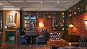 A library with bookshelves, leather armchairs, a fireplace, and a table. - Eurostars Montgomery (Brussels)