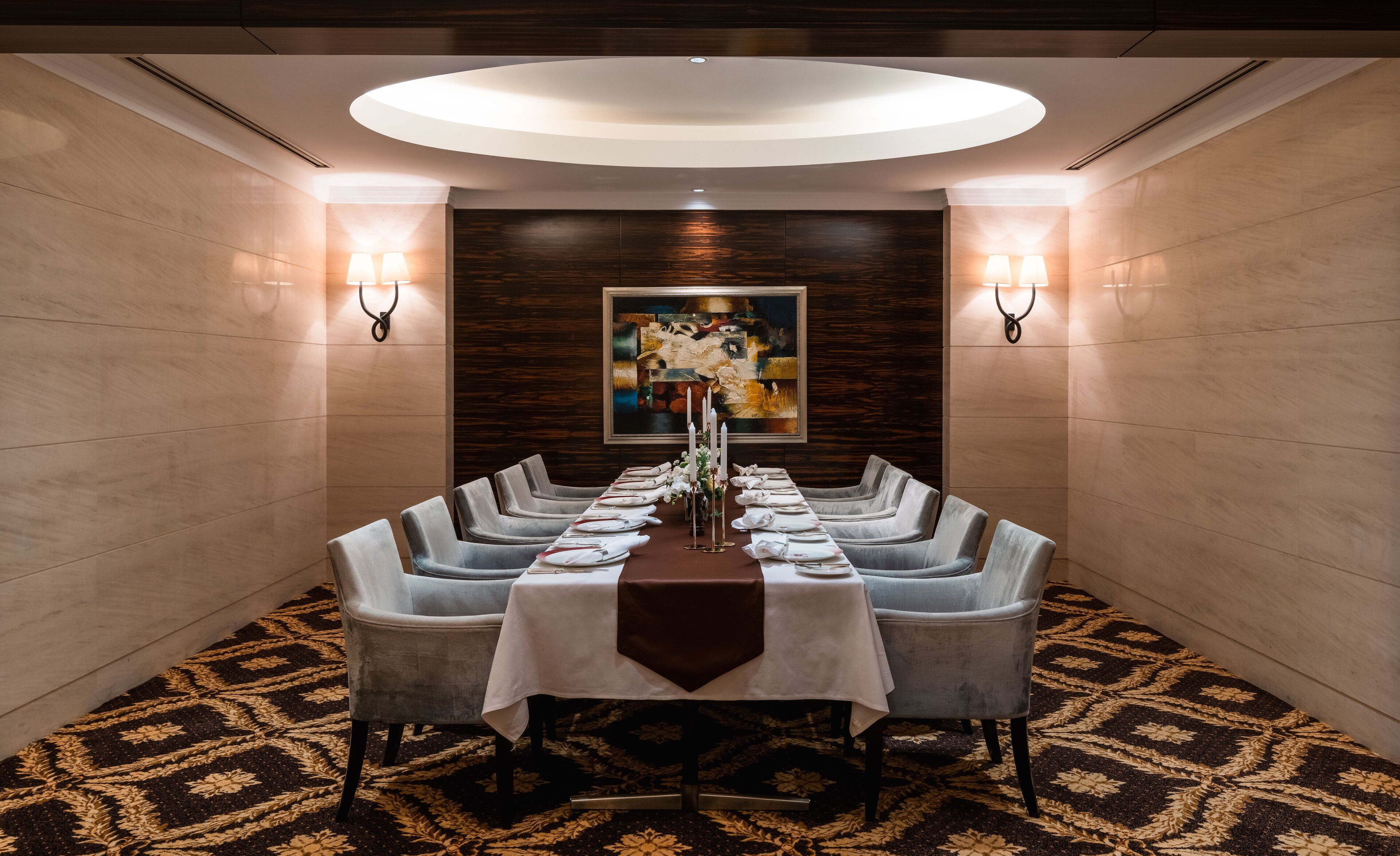 A formal dining room with a long table, grey upholstered chairs, a white tablecloth, and a large abstract painting on the wall.
