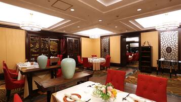 A hotel dining area with multiple tables, red upholstered chairs, and a large vase on one table.