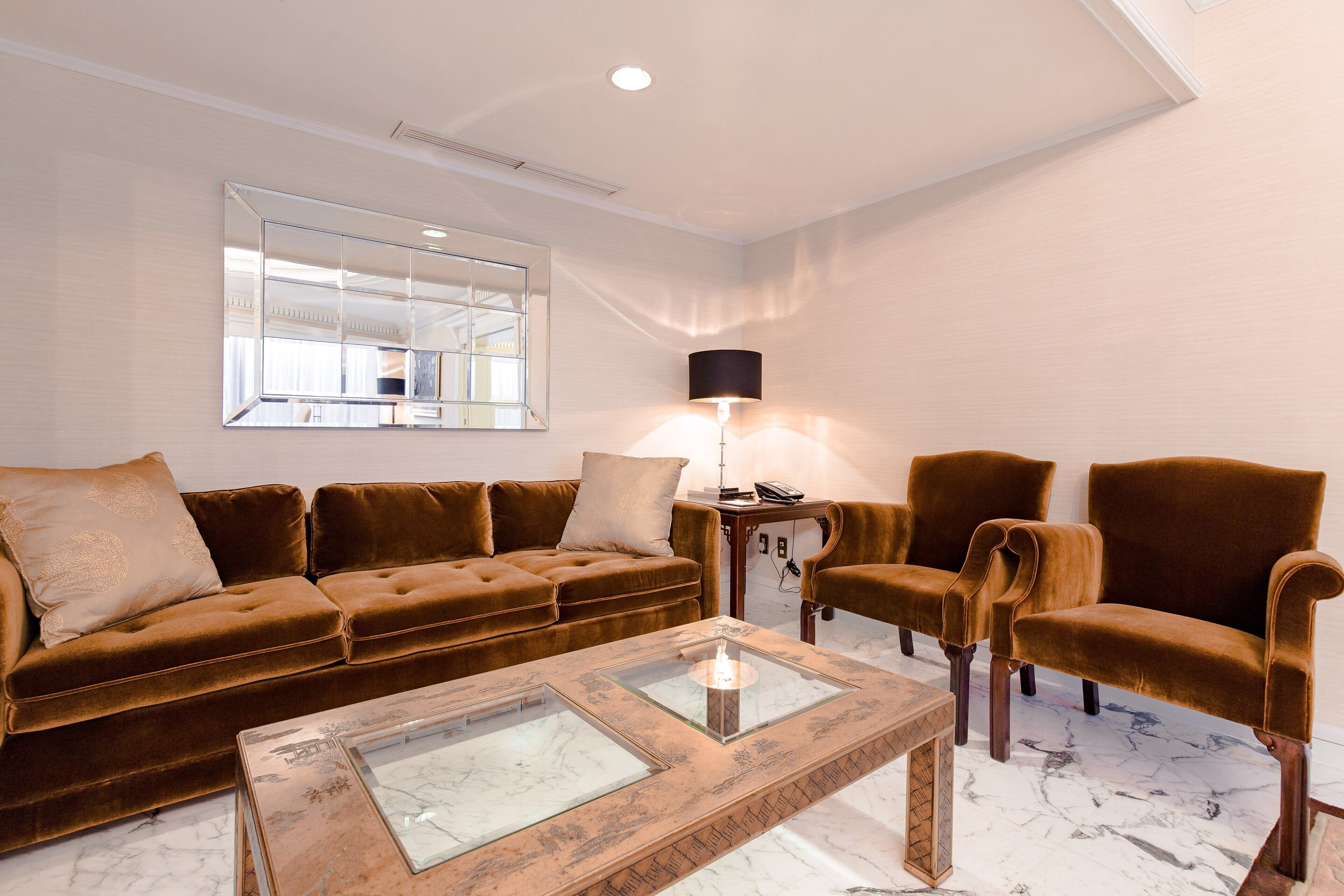 Una sala de estar moderna con un sofá de terciopelo marrón, dos sillones, una mesa de centro de vidrio y una lámpara de pie.