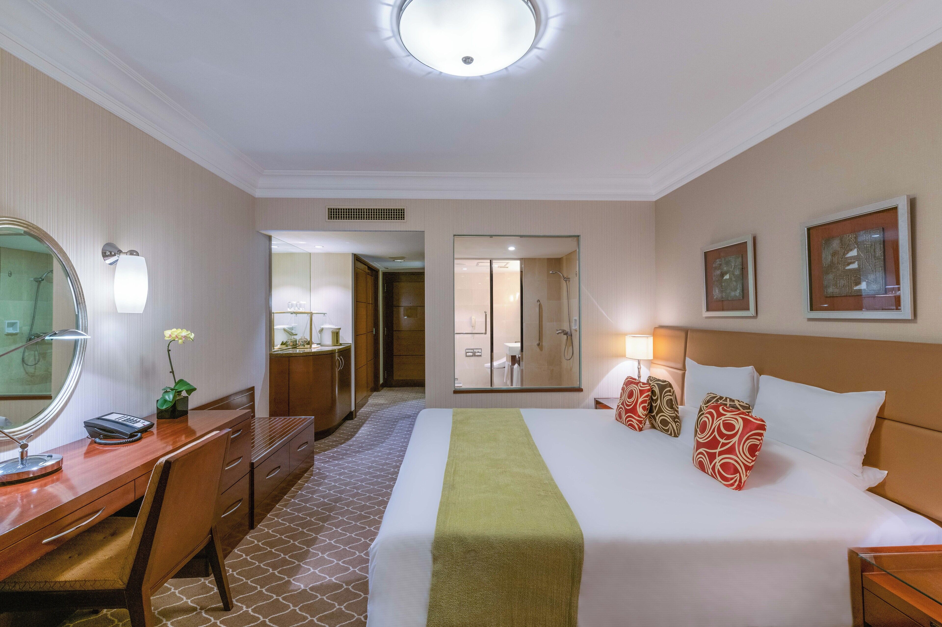 A hotel room with a bed, a desk, a mirror, a dresser, and a bathroom visible through a door.