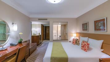 A hotel room with a bed, a desk, a mirror, a dresser, and a bathroom visible through a door.