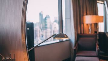 Una habitación con vista a un paisaje urbano a través de una ventana, una lámpara y un sillón.