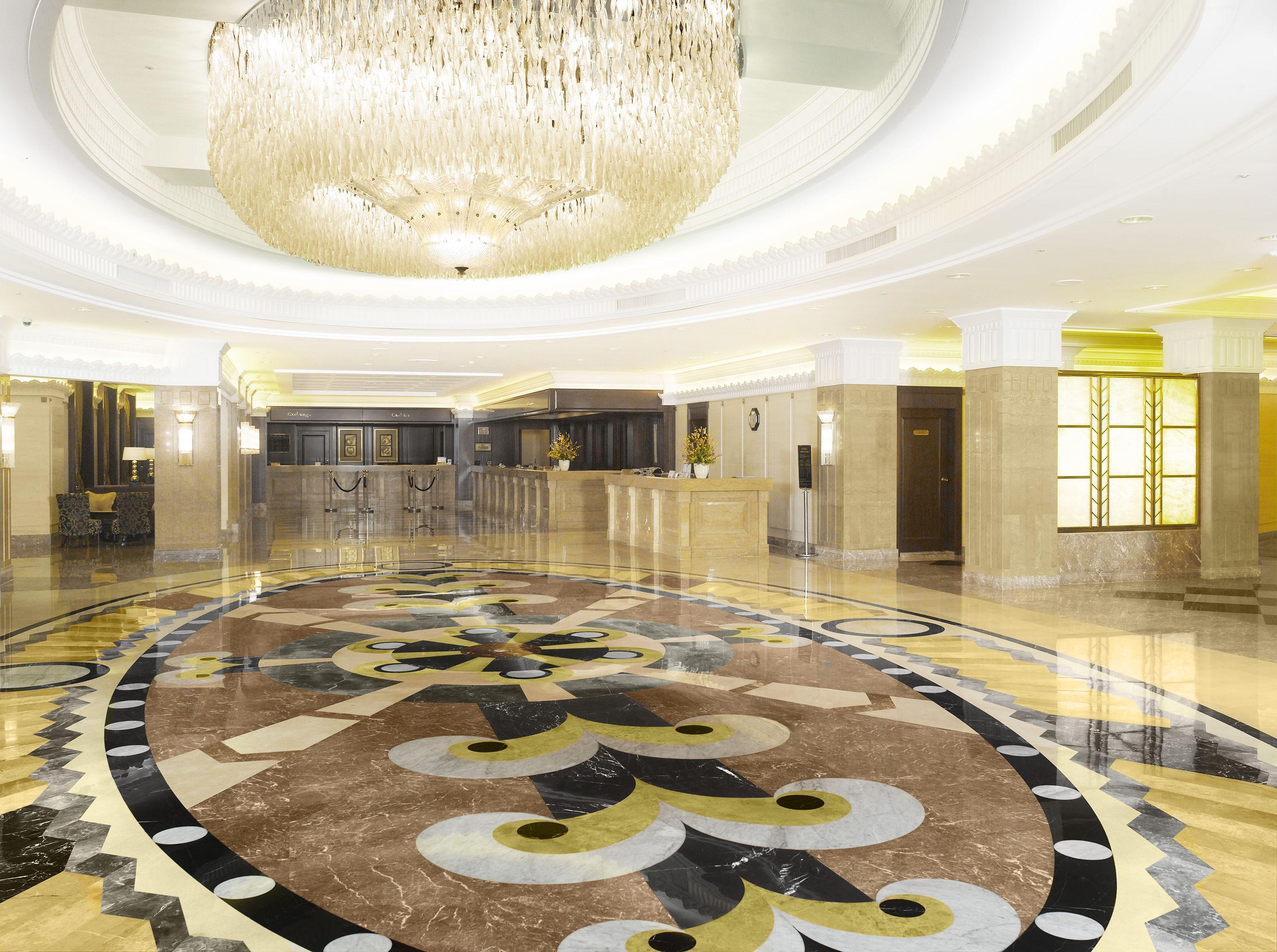 A spacious lobby with a large, ornate chandelier, a reception desk, and a patterned floor.