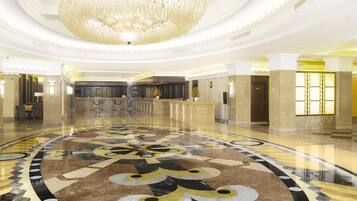 A spacious lobby with a large, ornate chandelier, a reception desk, and a patterned floor.