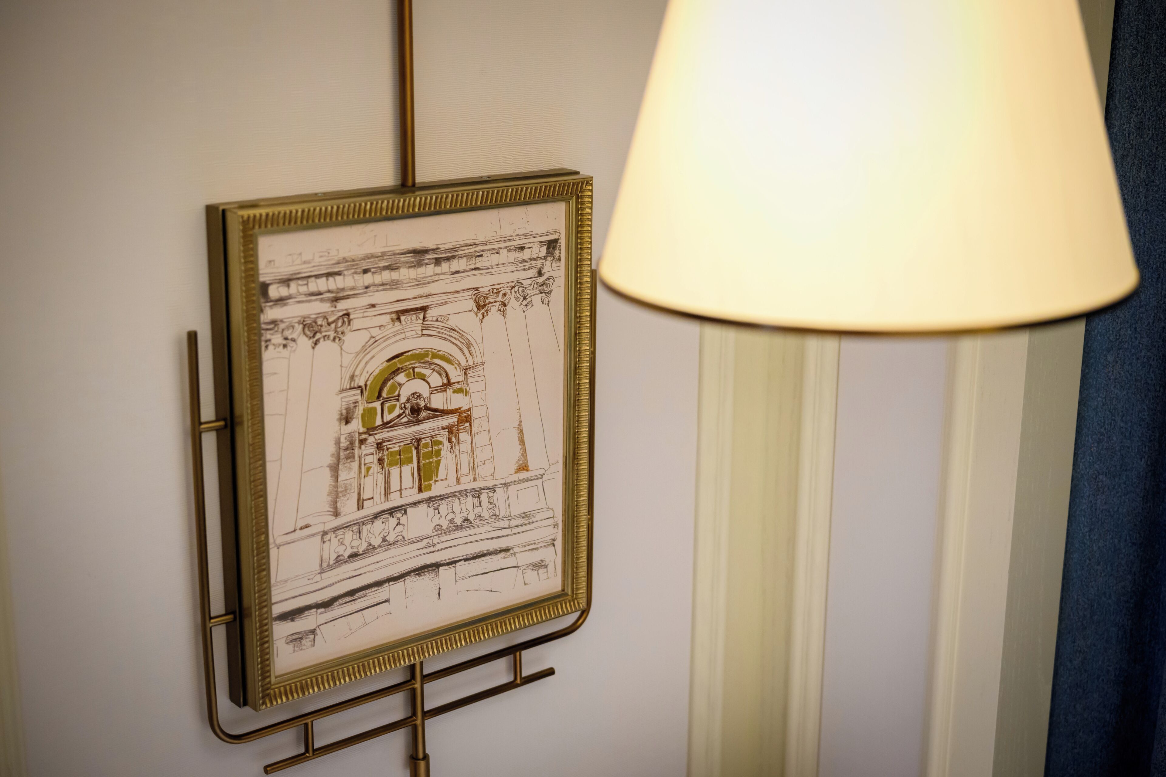 A framed architectural sketch on a wall, a lamp, and a curtain.